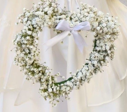 Cuore di gypsophila con fiocco di raso bianco, tenuto davanti a un abito bianco