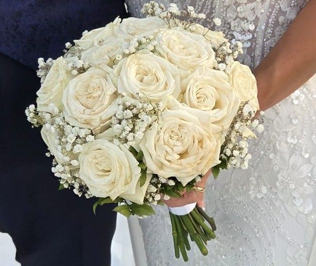 Bouquet da sposa tondo di rose bianche e gypsophila tra le mani della sposa in abito ricamato