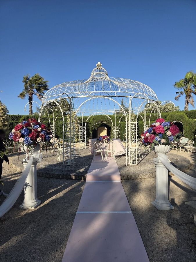 Allestimento di cerimonia all'aperto con gazebo bianco, passatoia rosa e colonne con vasi di ortensie colorate