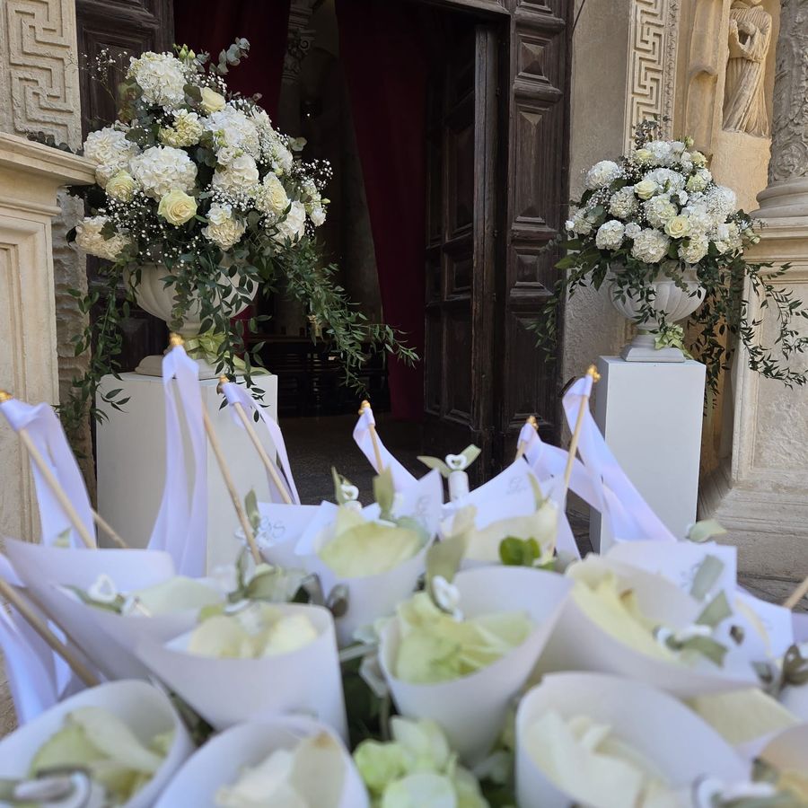 Ingresso di chiesa addobbato con vasi di ortensie e rose bianche su colonne e coni portapetali con le iniziali degli sposi