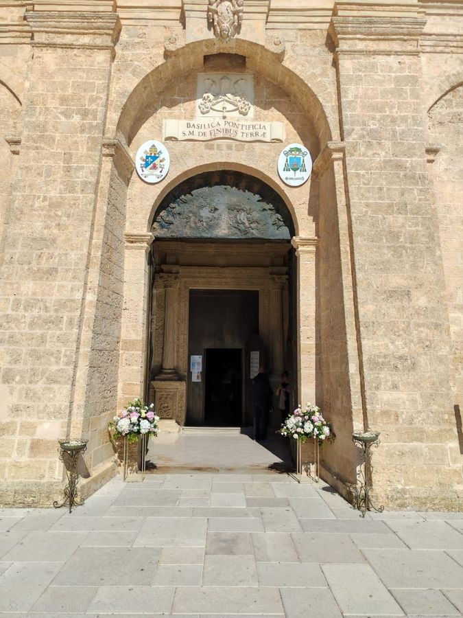 Ingresso di basilica in pietra leccese addobbato con due composizioni su alzata di rose bianche e rosa e fiori di campo