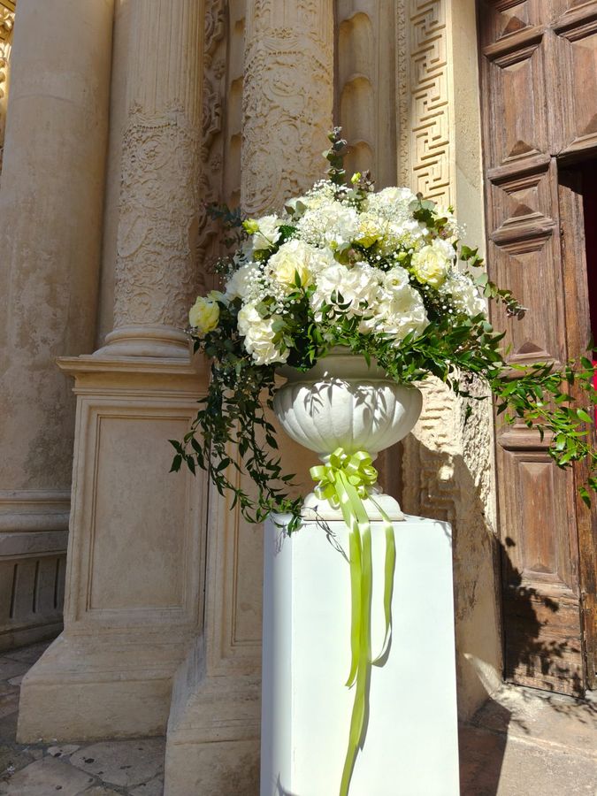 Alzata floreale bianca con ortensie, rose e gypsophila su colonnina all'ingresso di una chiesa barocca