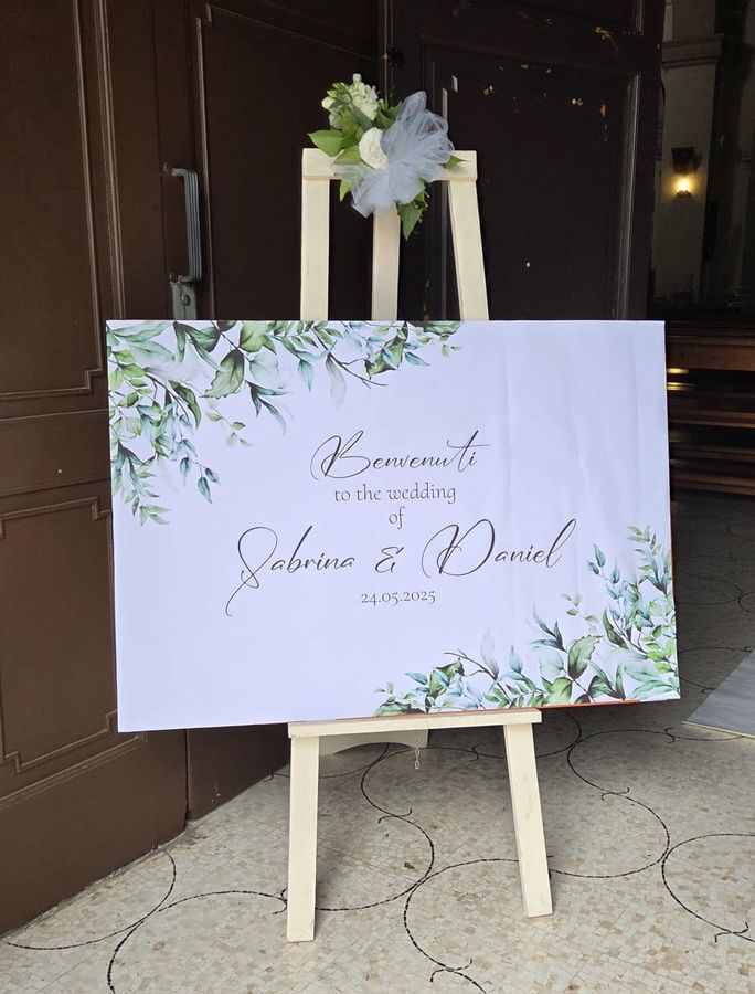 Cartello di benvenuto per matrimonio su cavalletto in legno, decorato con rose bianche e tulle all'ingresso della chiesa